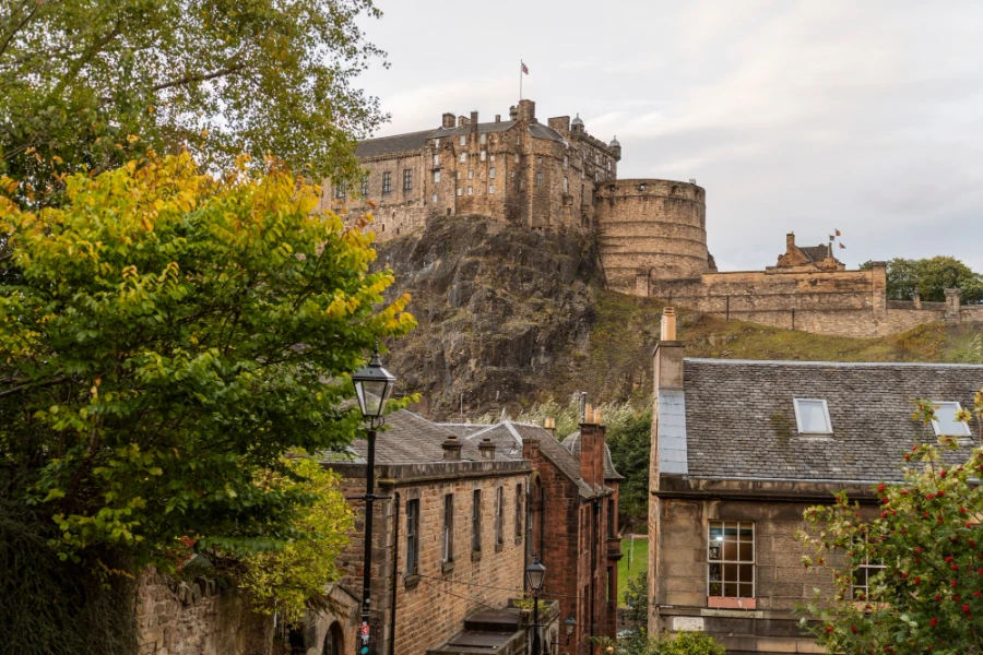 Edinburgh Castle atop a cliff with stone brick buildings in the foreground