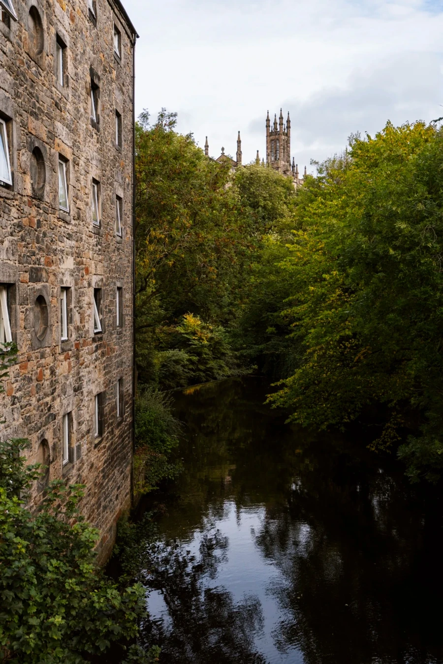 A tall stone building extends directly out of the water by The Water of Leith Walkway