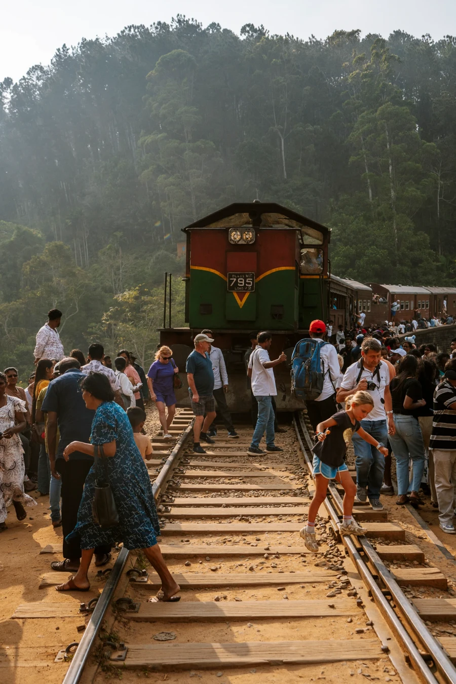 A crowd scatters across the tracks in frontt of a train on the iconic nine arch bridge in Ella