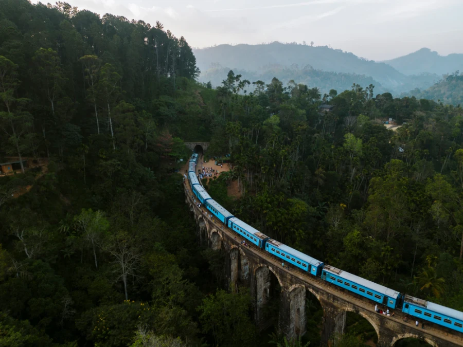 A massive blue train crosse the nine arch bridge above the dense jungle in Ella, Sri Lanka
