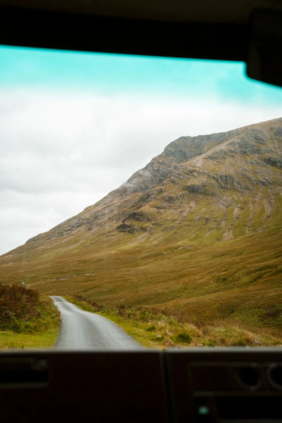 A narrow single track road disappears around a corner on the way to Loch Etive near Glencoe, Scotland