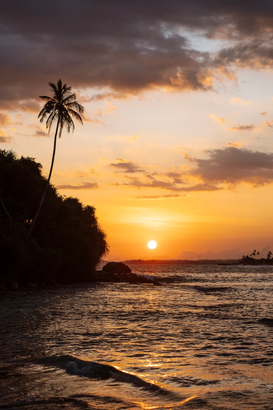 The sun hangs just above the horizon casting a warm glow on the calm waters of Dickwella Beach