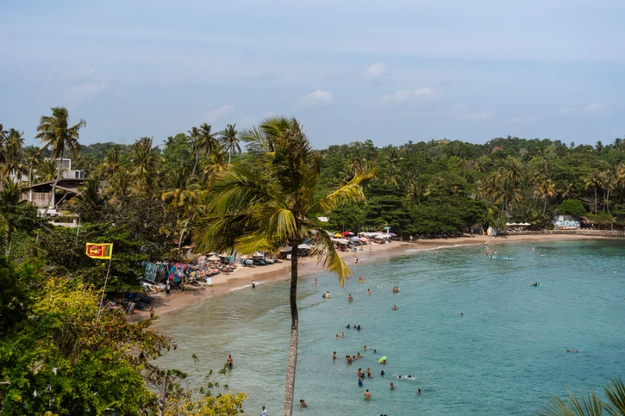 Crowds of people swimming and surfing in the protected cove of Hiriketiya Beach