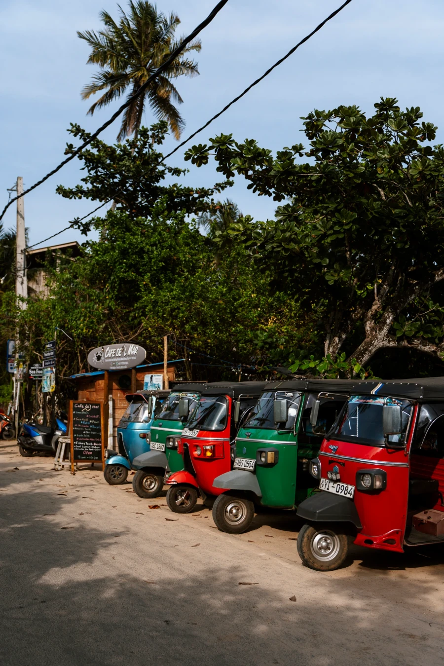 A row of multi colored tuktuks parked along a sandy road near Hiriketiya Beach in Sri Lanka