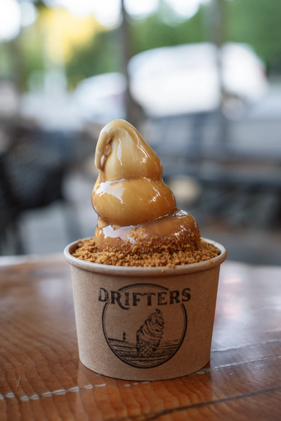 A cardboard cup overflowing with soft serve ice cream drizzled with espresso sauce and Biscoff crumble