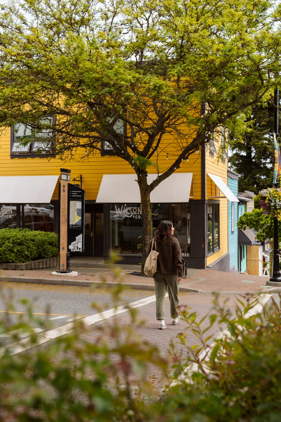 A woman crossing the street with a yellow building across the street