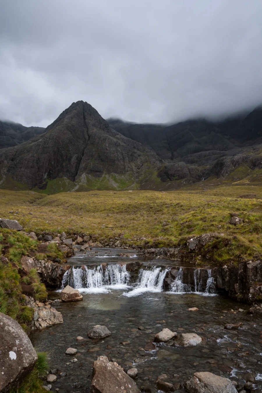 A small waterfall cascades over a short drop into a pool of water at the Fairy Pools on The Isle of Skye
