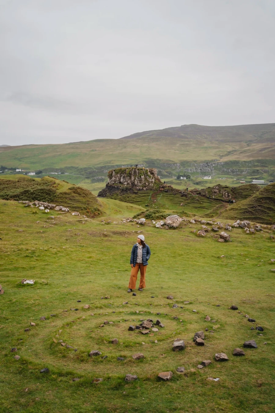 A woman stands in front of a spiral shape made of stones in the Fairy Glen The Isle of Skye, Scotland