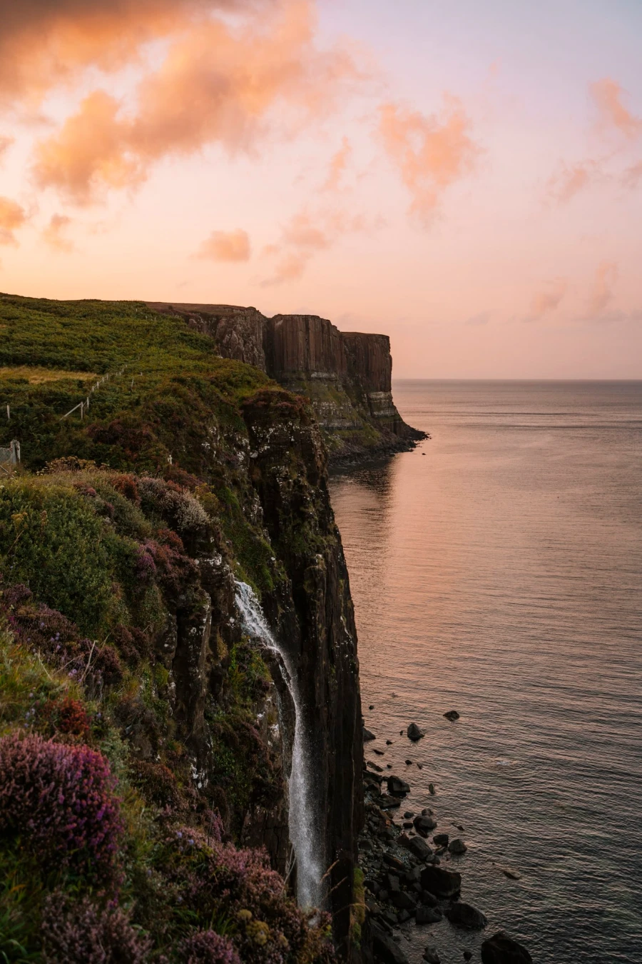 Mealt Falls pours off of a cliff and falls into the sea why the whispy clouds in the sky glow orange in the sunset light
