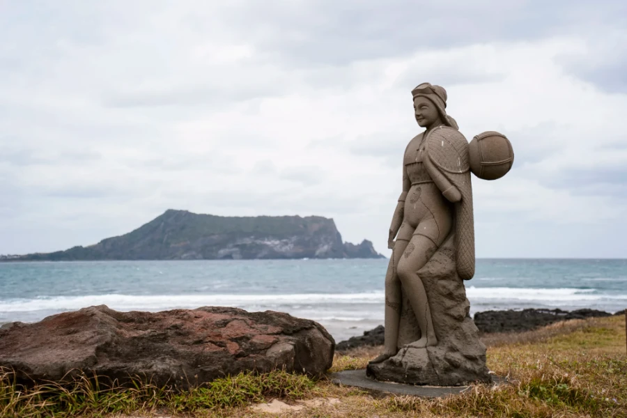 A stone statue of a Haenyeo woman sits on the coast of Jeju island