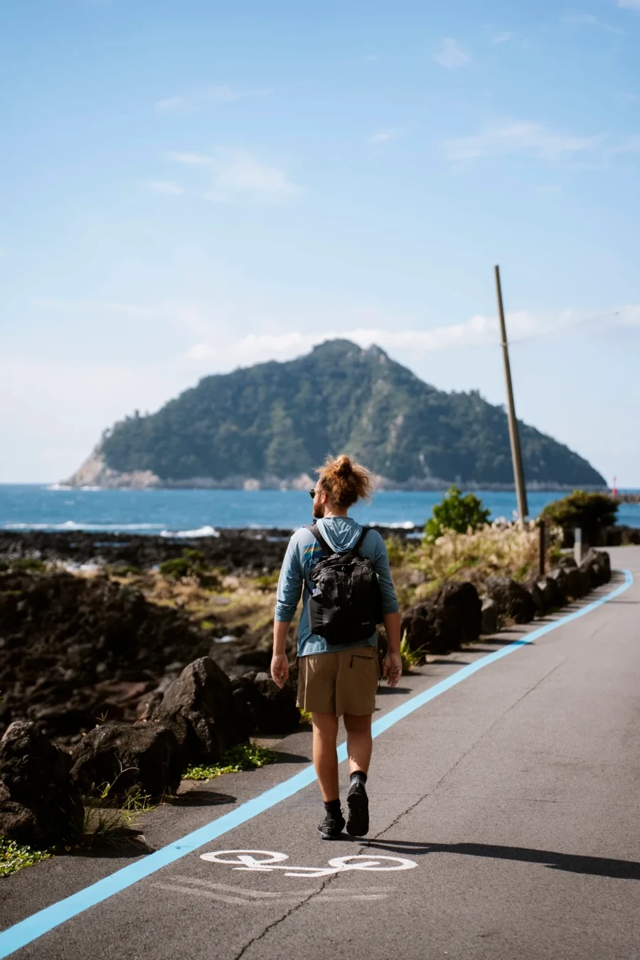 man walks along a hiking trail on Jeju island with a distant island visible behind him
