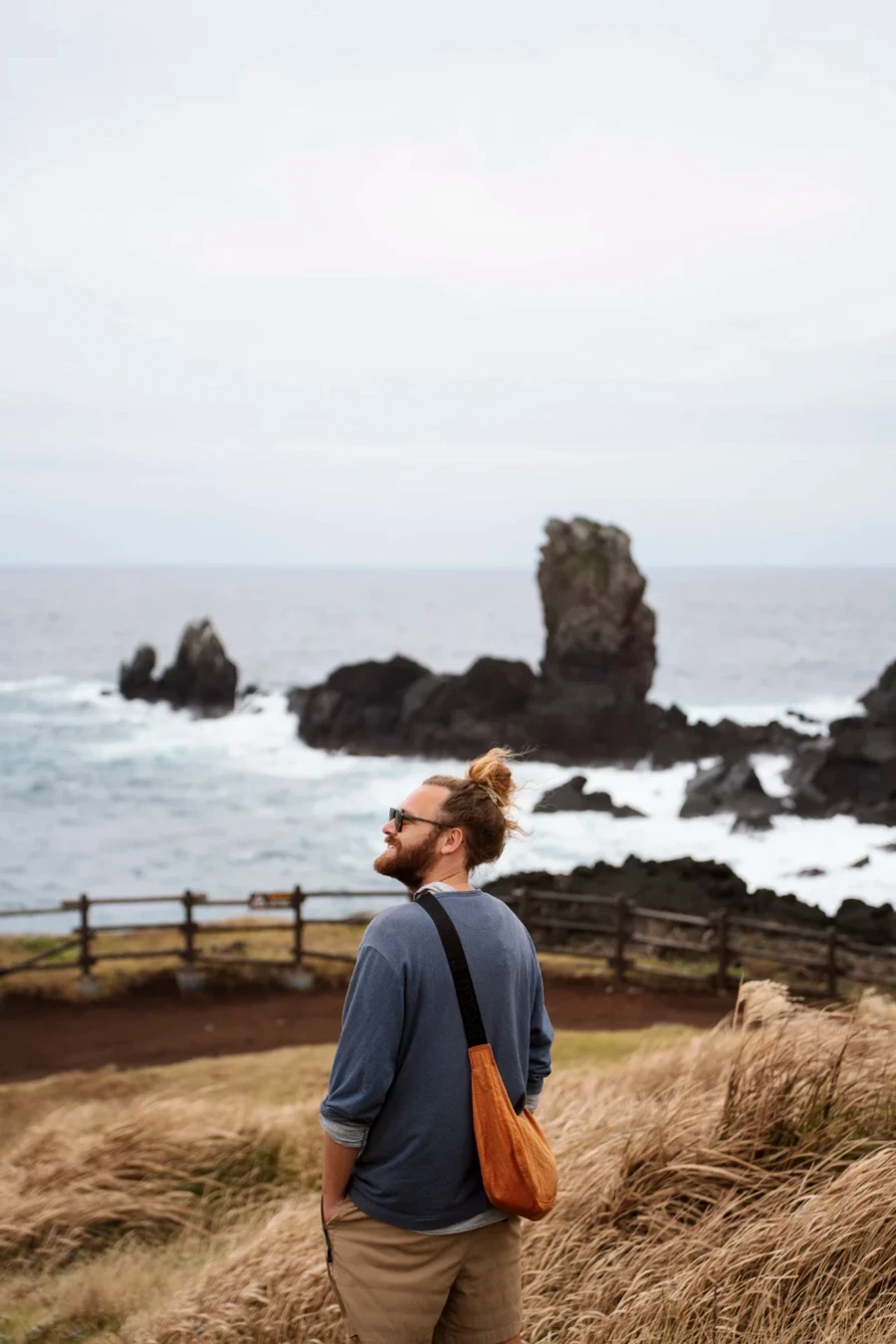 man stands looking out to rocky pillars that rise out of a choppy sea on the coast of Jeju Island