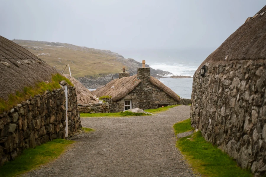 A gravel path leads between two traditional stone houses in Gearrannan Blackhouse Village