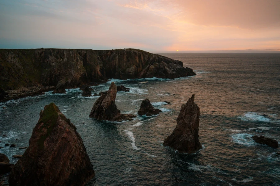Sharp rocky pillars known as the Mangersta Sea Stacks stick abruptly out of choppy seas with steep cliffs in the background