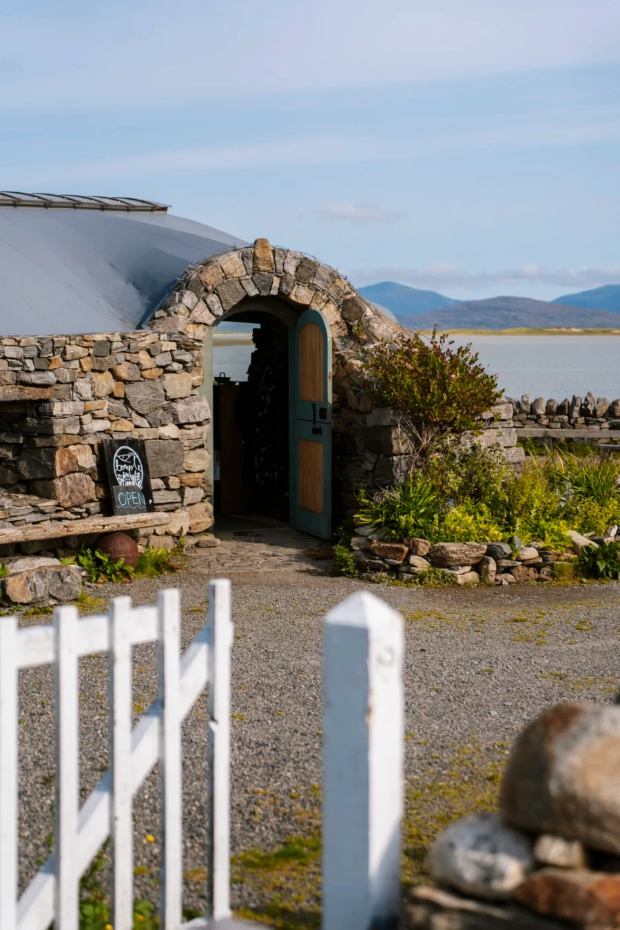 A white picket fence gate and a stone archway lead into Temple Harris, on the Isle of Lewis and Harris