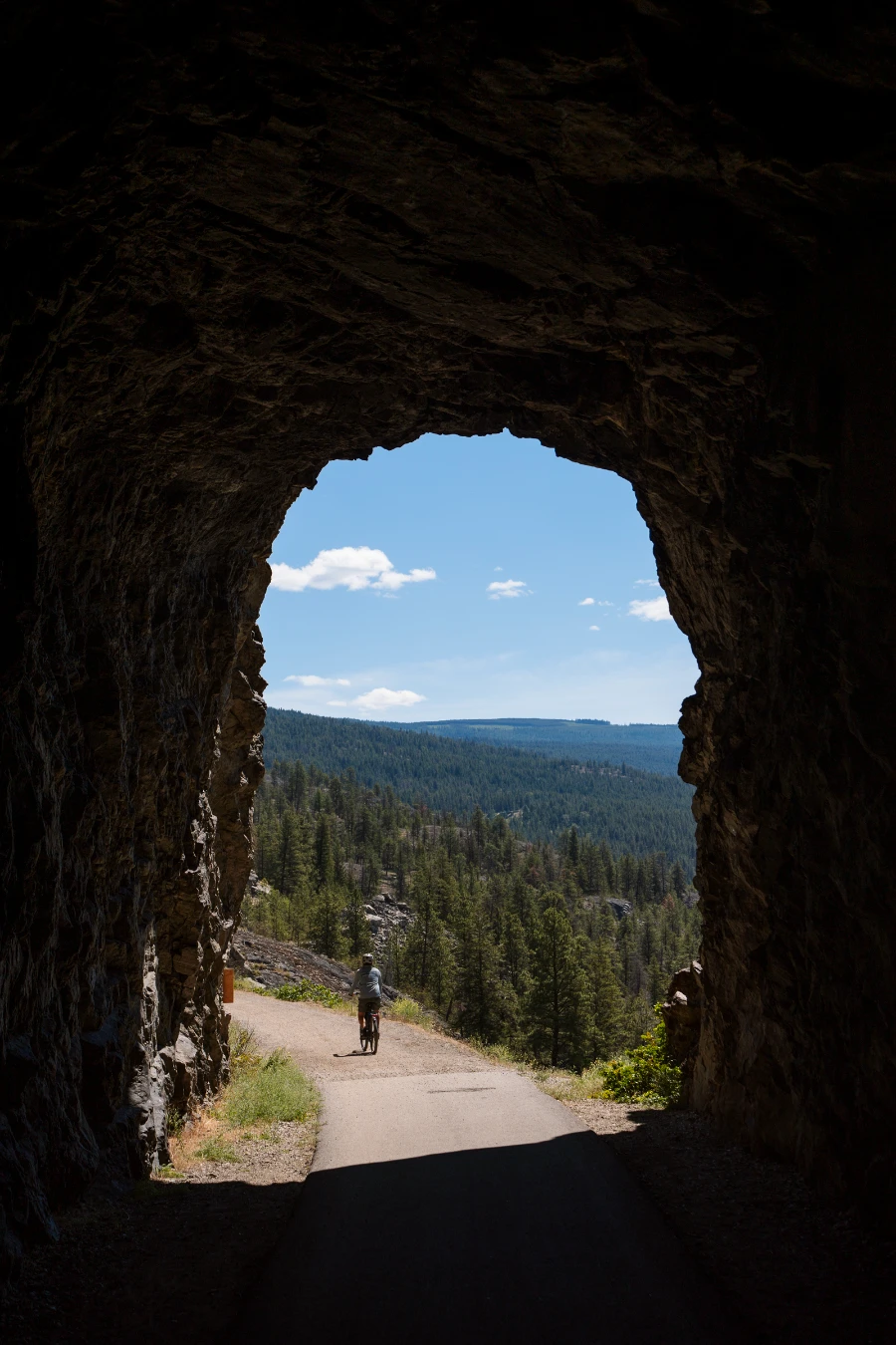 A man rides out of the darkness of ‘Little Tunnel’ and into the light cast on the trail and the massive sea of forest below the trail.