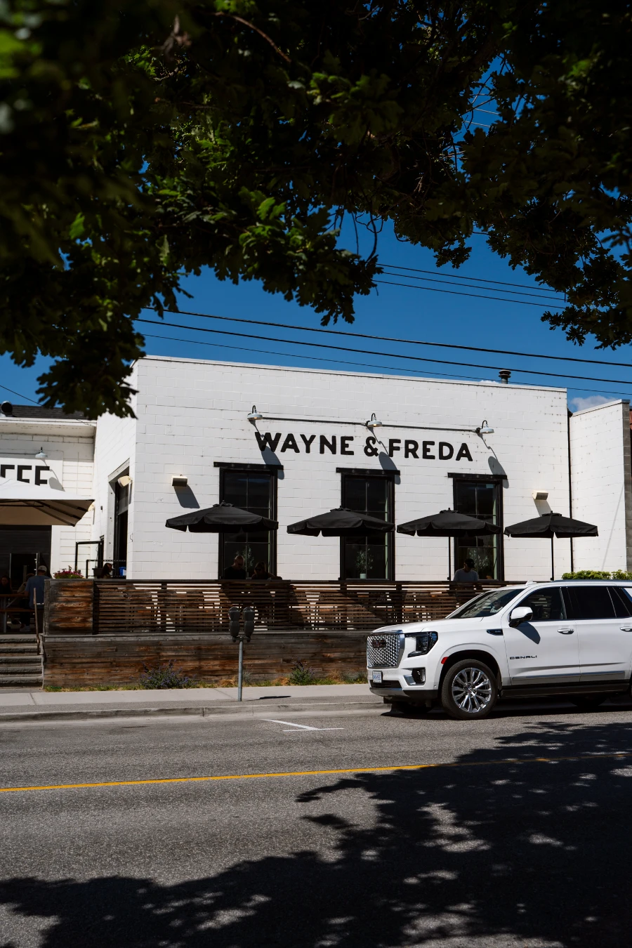 A white stone building with an outdoor patio with several umbrellas-covered tables has the words ‘Wayne & Freda’ written on the side with black paint.