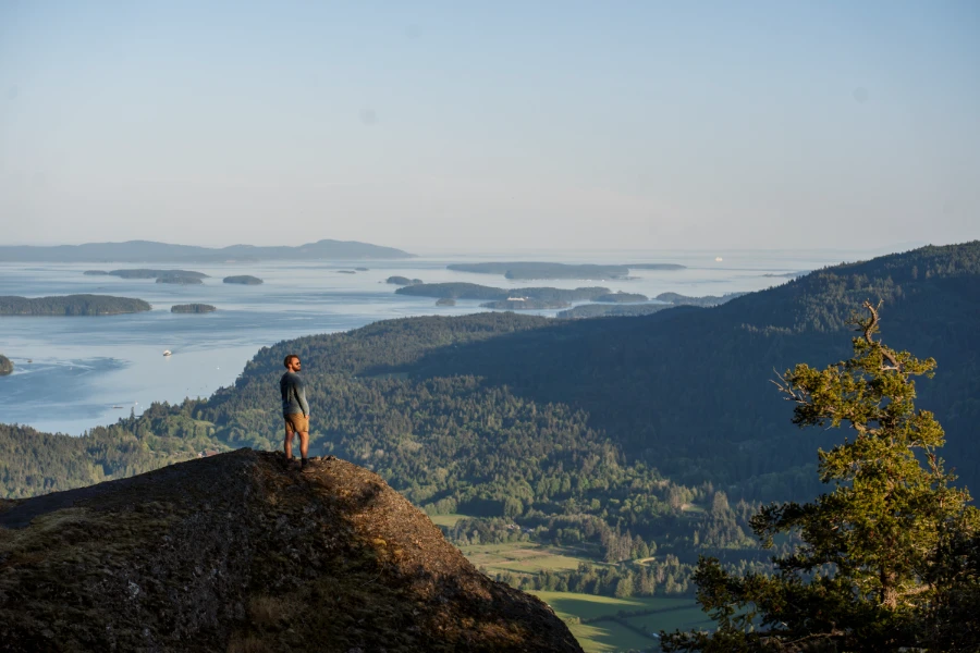 A man stands on a cliff near the peak of Mount Maxwell high above the lush green valley on Salt Spring Island