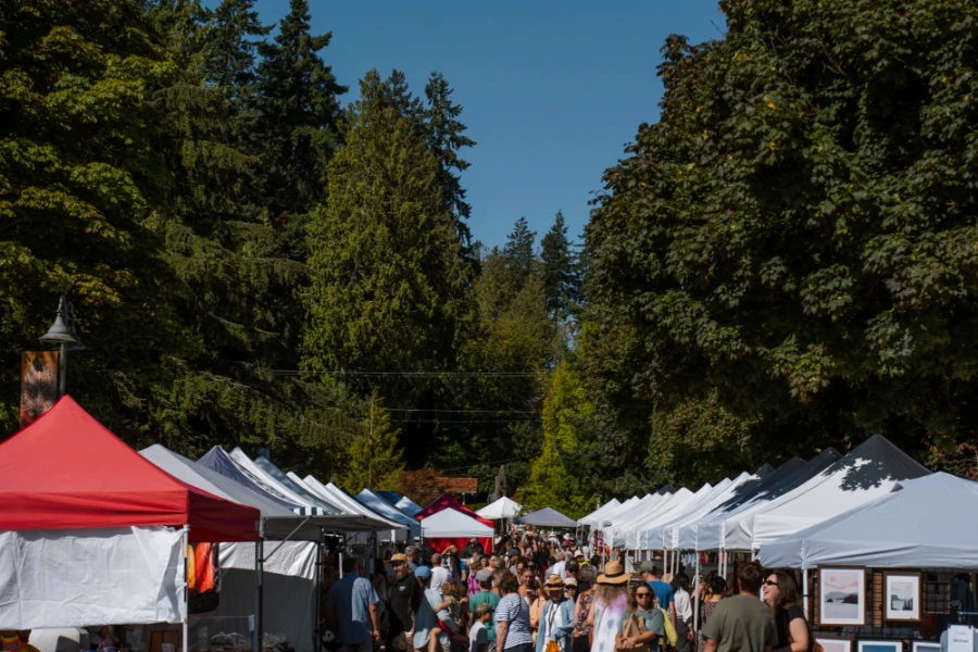Two rows of white tent with a crowd moving between them at the Sechelt Farmers Market in BC