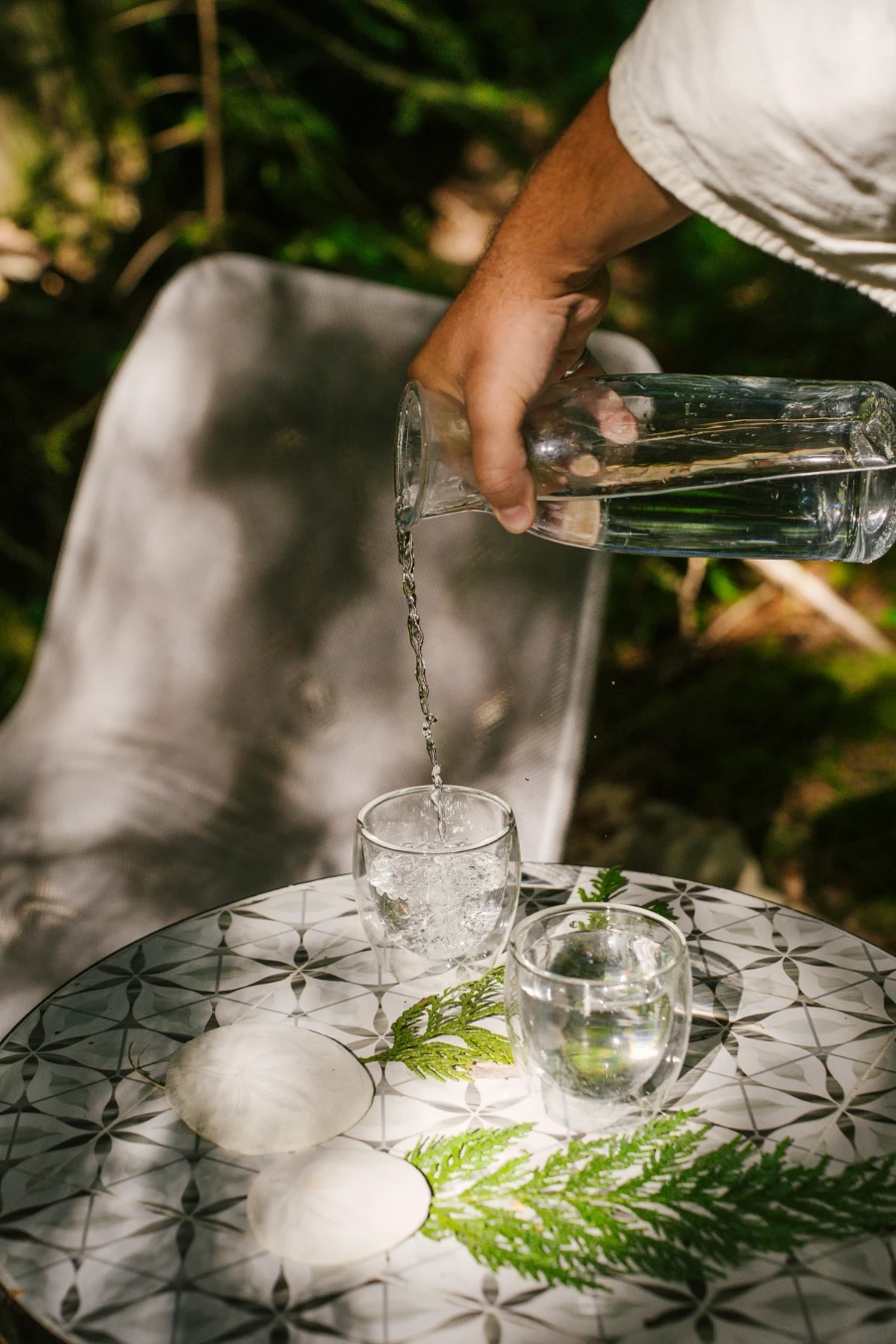 Water pouring from a vase into a clear glass set on a table with decorative ferns