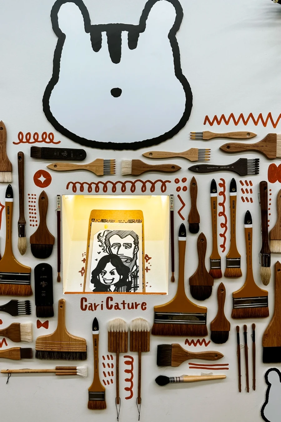A caricature of a man and a woman is placed at the centre of a collection of varying sized paint brushes