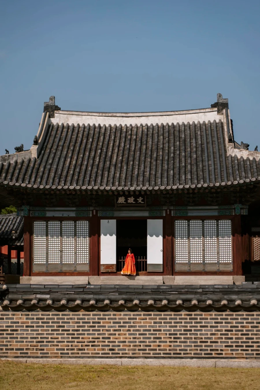 Woman in a traditional orange dress stands in a building entrance at Changgyeonggung Palace, Seoul
