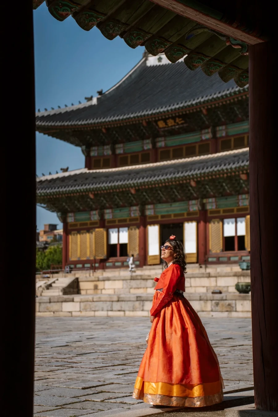 Woman in a traditional orange dress stands in front of a Korean temple at Changgyeonggung Palace, Seoul