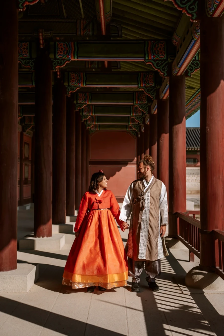 A man and woman dressed in traditional Hanbok holding hands walking through Gyeonbokgung Palace