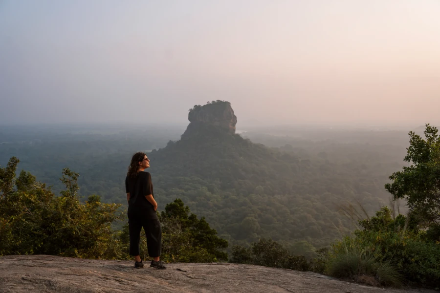 portrait of a woman standing at a cliffs edge with lions rock in the background