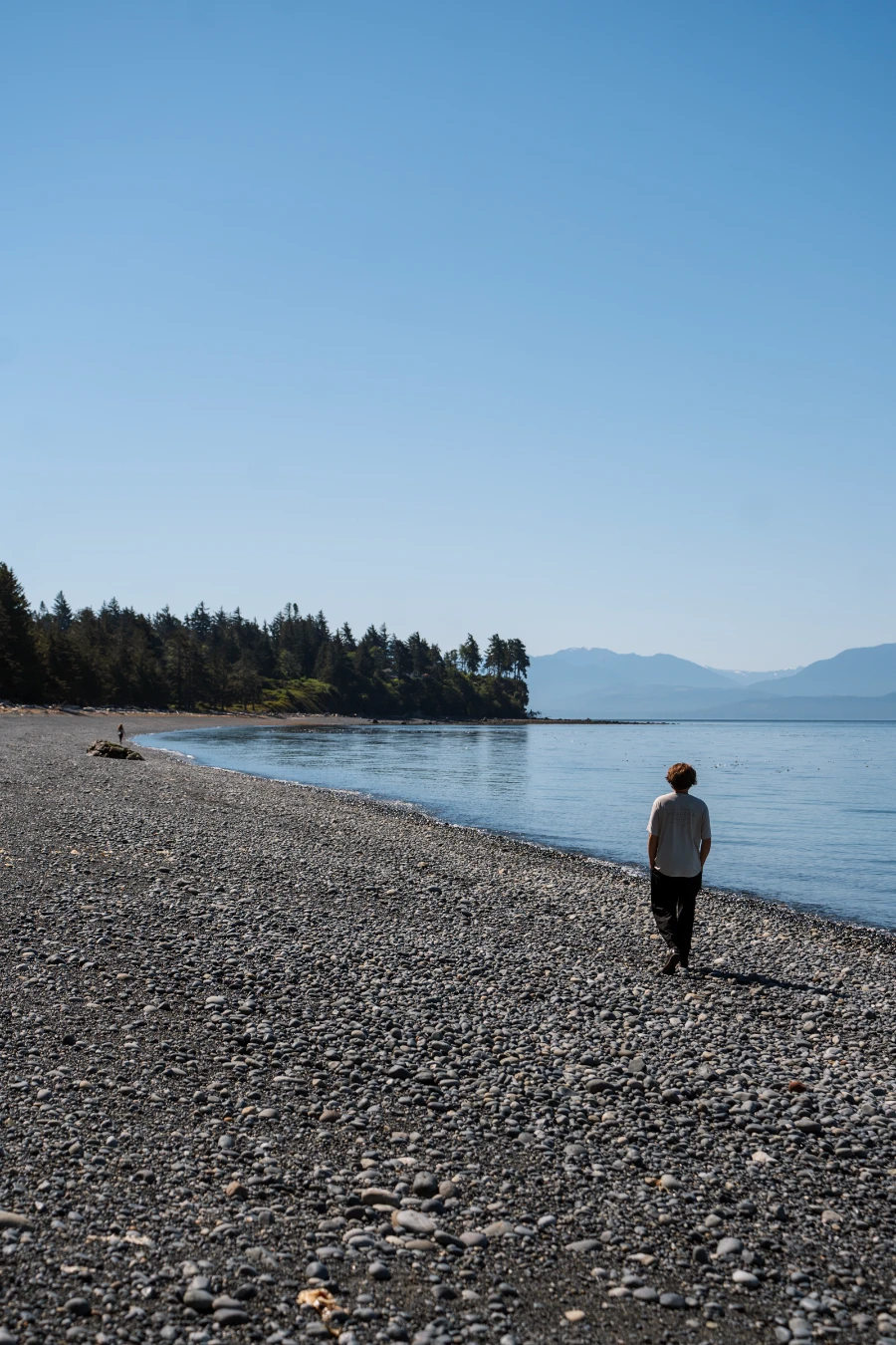 A man walks along a rocky beach next to a calm sea