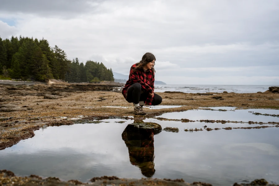 A woman stoops next to a tidal pool creating a clear reflection in the water
