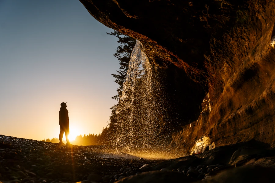 A steady stream of water pouring over a sandstone cliff onto the rocky beach below