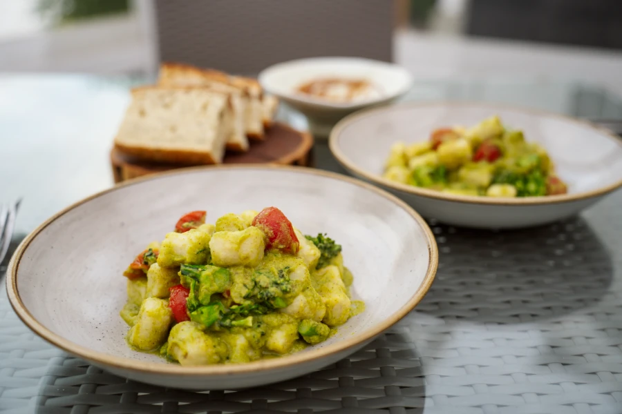 Two plates of pesto gnochi sit on in bowels on a glass table