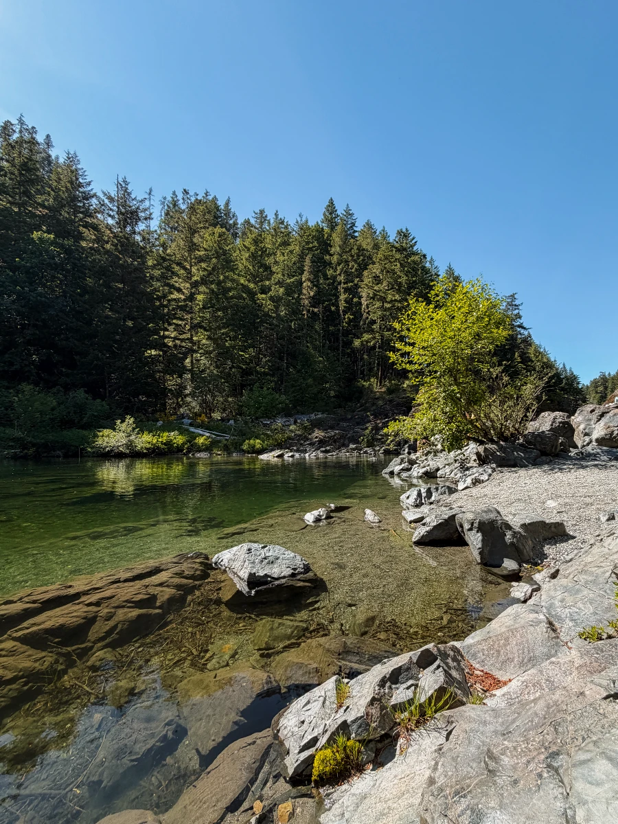 A flat rock shelf lines a calm turquoise river in Sooke Potholes Provincial Park