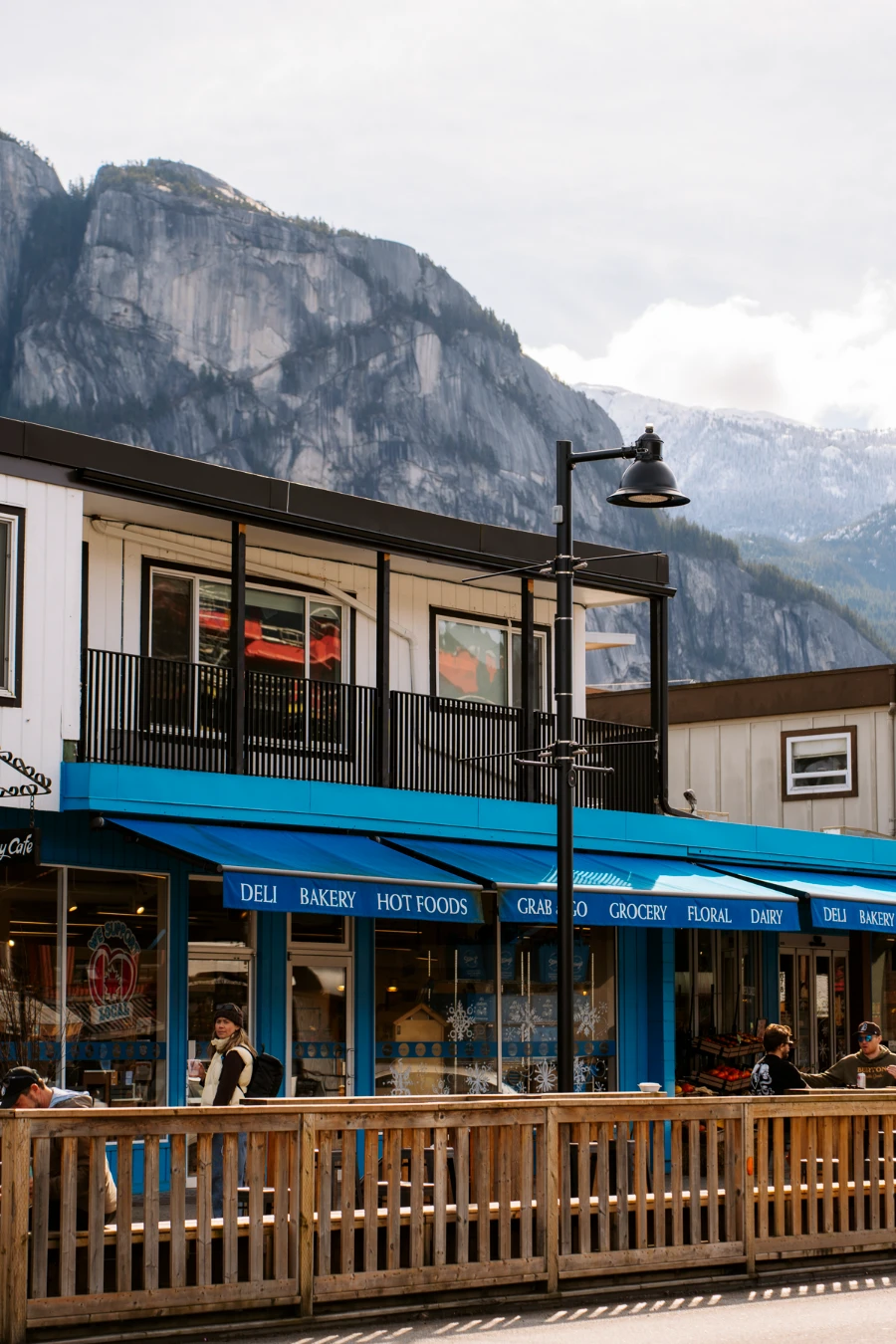 A wooden fence closes in a roadside patio with storefronts behind them and the chief behind the storefronts towering over town