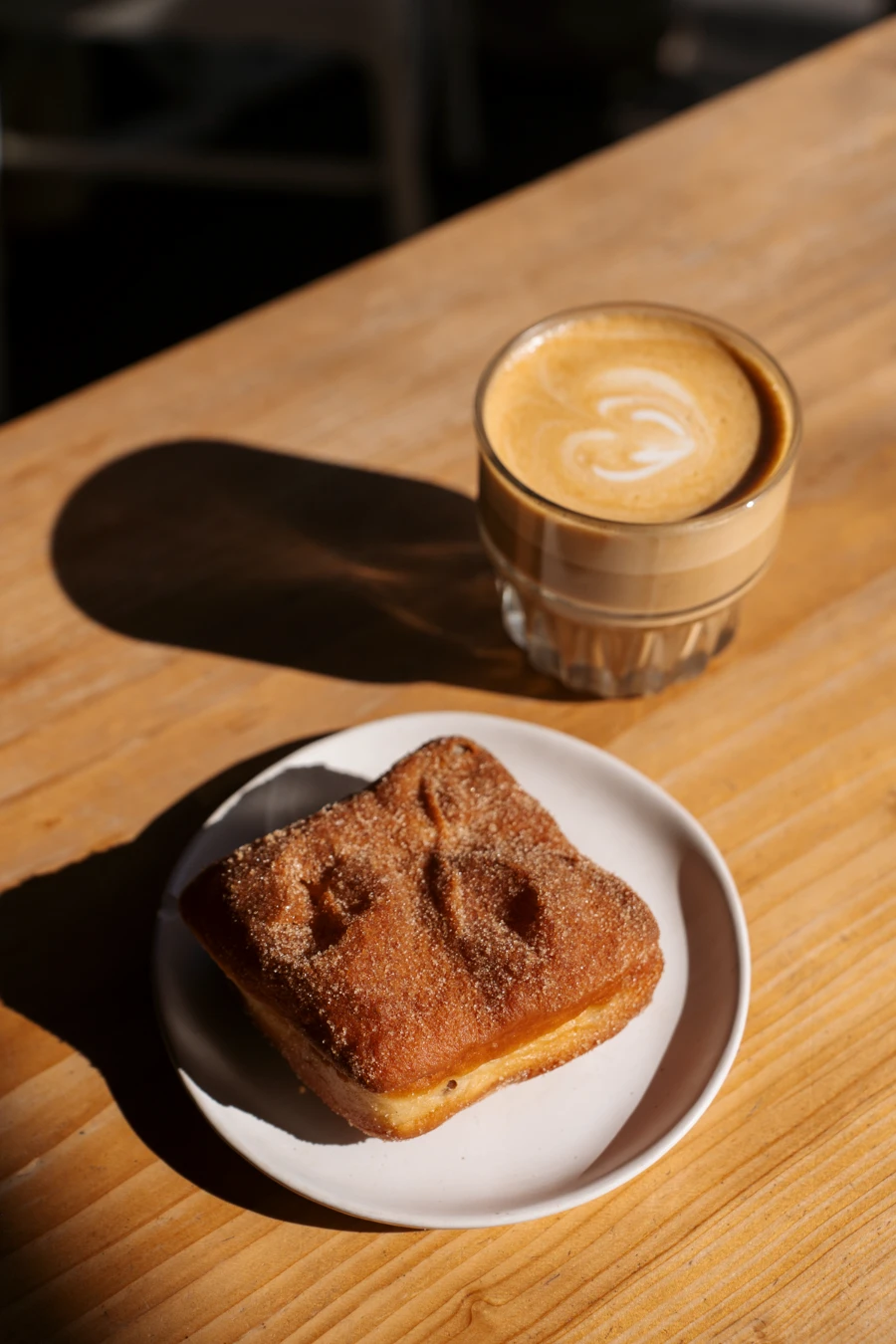 A coffee and a square-shaped donut are set on a wooden table on the Fox and Oak patio in Squamish