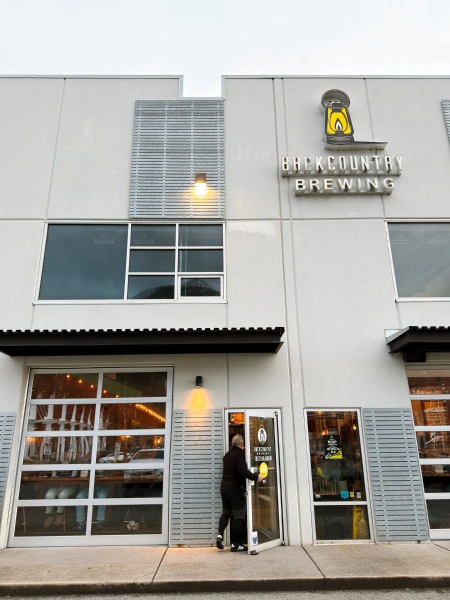 A man opening a door and walking into the industrial-looking facade of Back Country Brewing
