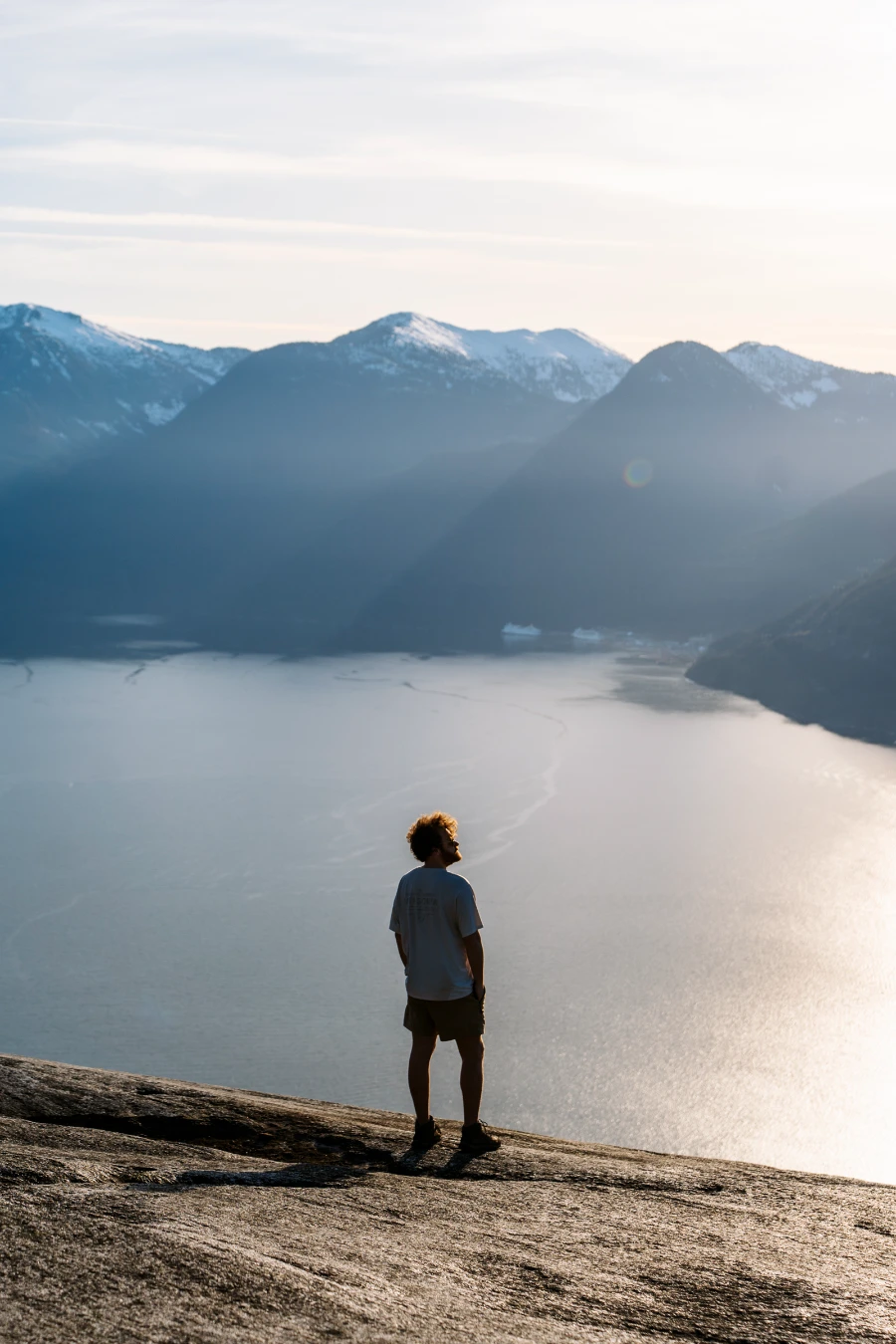 A man stands on the bare granite cliff faces of the Stawamus Chief with the Sea to Sky Highway running beneath it.