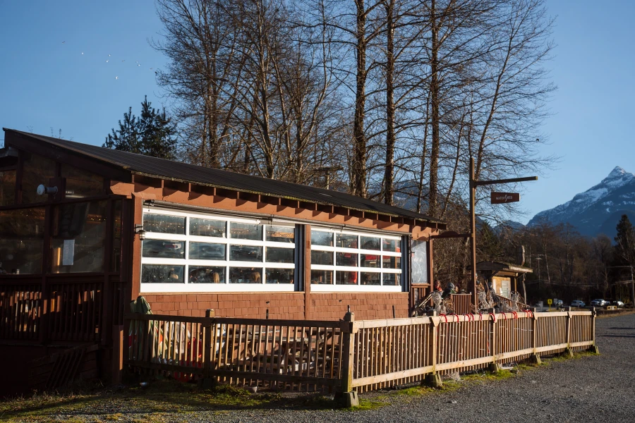 A wooden fence contains a patio with picnic tables just outside of the Watershed Grill that is built along Eagle Run Path in Squamish