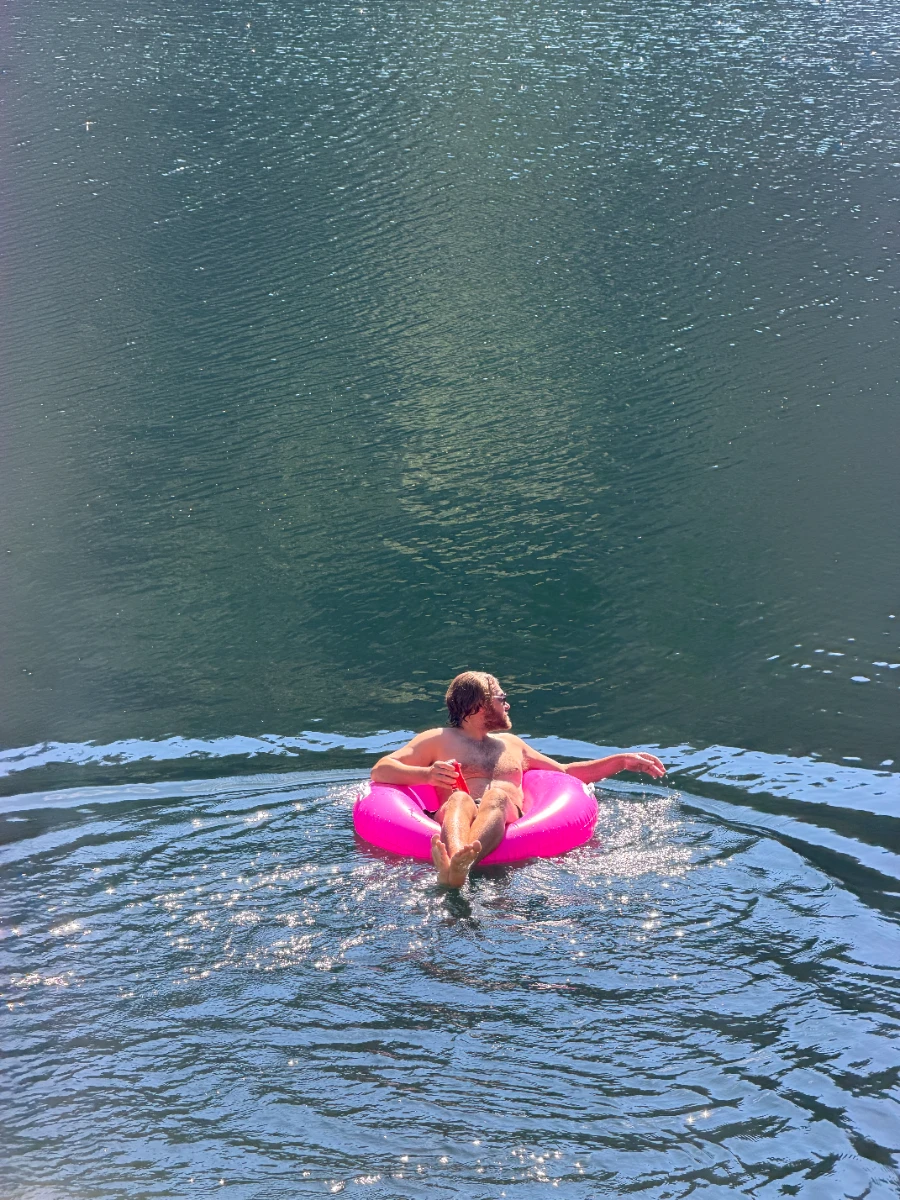 A man holding a beer and floating in a pink circular inflatable floaty in a lake just outside of Squamish