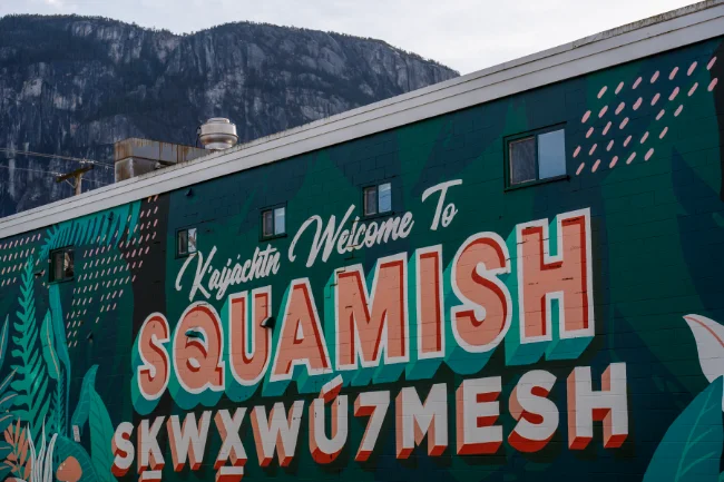 A woman stands on a bare rock face looking out at the south face of the Stawamus Chief in Squamish