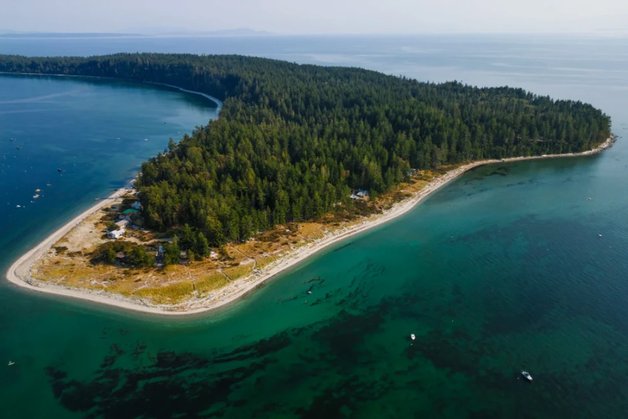 A horseshoe shaped beach wraps around an island covered entirely in trees at the southern side of Savary Island off of the Sunshine Coast, BC