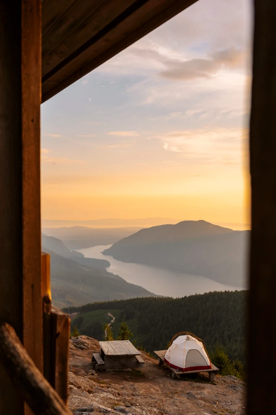 A picnic table and a tent set up on a wooden tent pad with a clear view looking down the the valley and river below