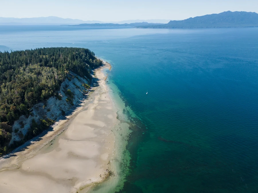 Expansive sandy stretch of Vaucroft Beach with steep cliffs climbing to the left and the water stretching to the right toward Vancouver Island on the horizon