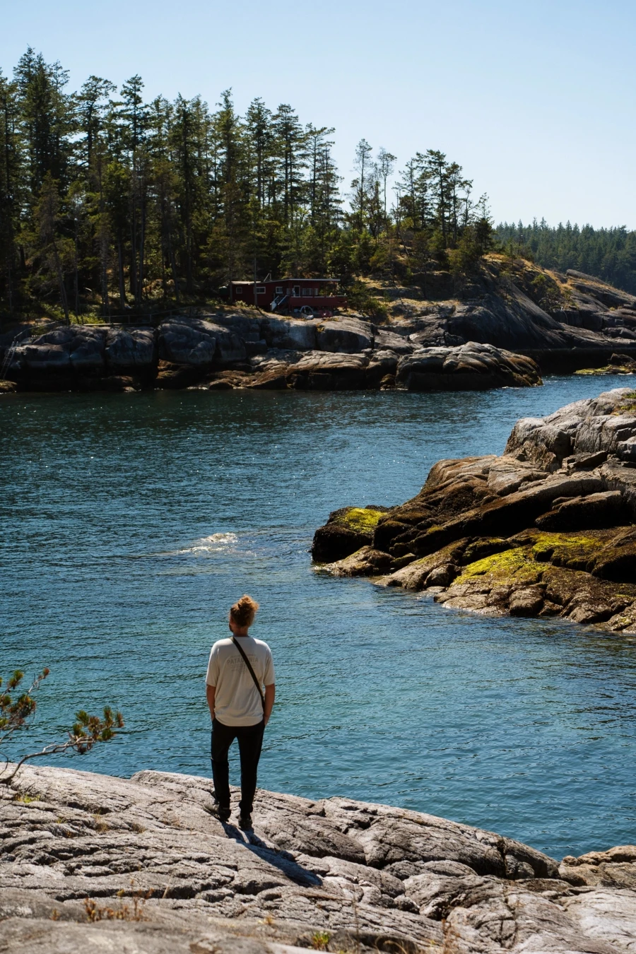 A man stands on the rocky shore above  the parkling water along the rocky coast of Smugglers Cove near Sechelt, BC