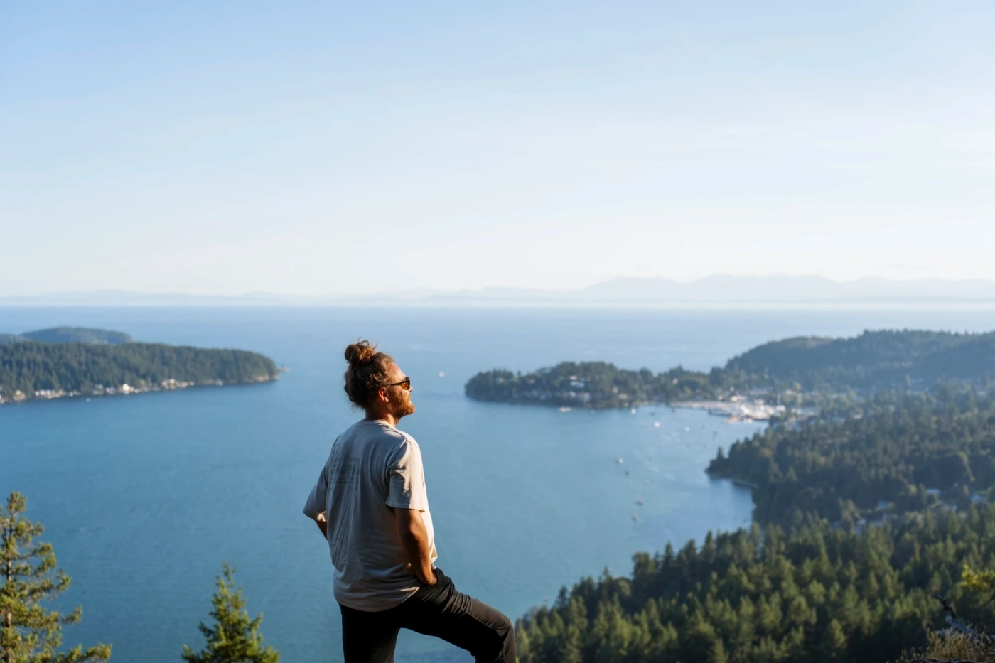A man stands at the top of Soames Hill with several forested islands dotting the water below him.