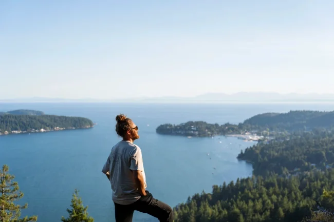 A man stands at the top of Soames Hill with several forested islands dotting the water below him.