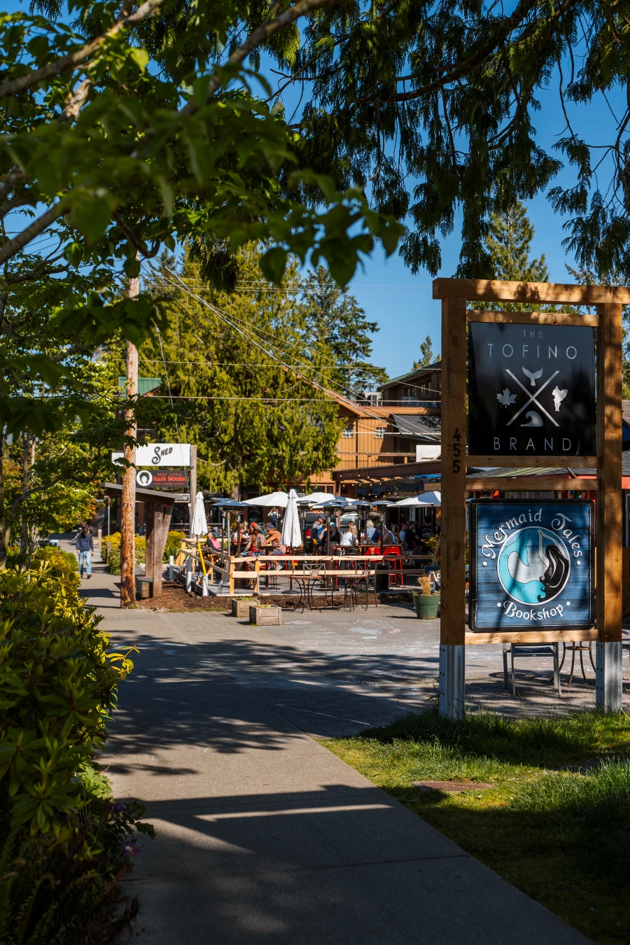 An empty side walk lined with signs and busy patios in Tofino, BC