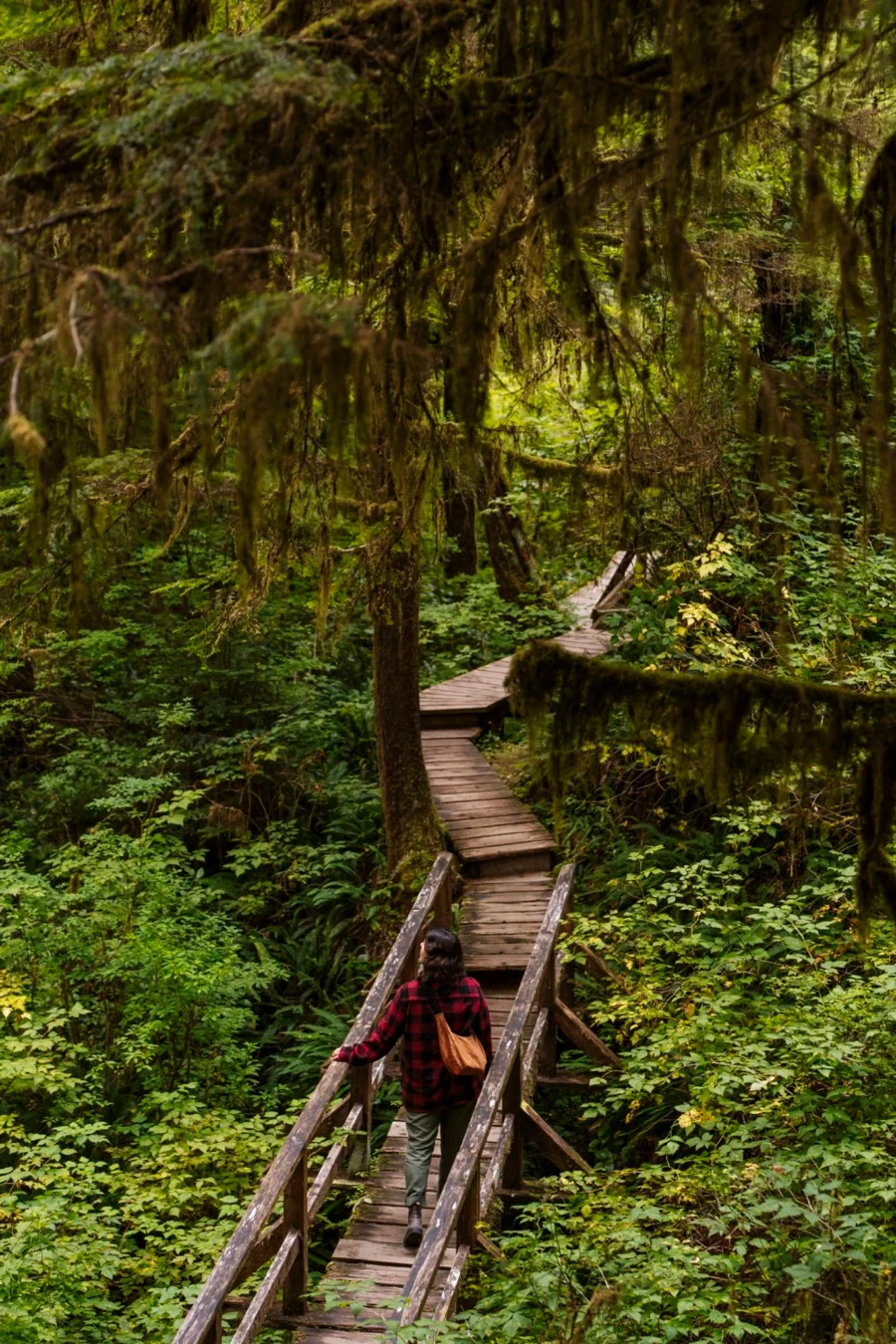 woman in a red flannel jacket walking along a wooden boardwalk in Pacific Rim National Park, Tofino, BC