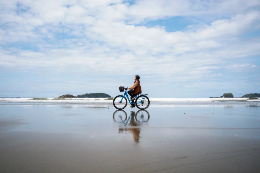 woman riding a bike along the wet sand at low tide on Long Beach in Tofino, BC